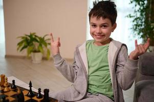 feliz Adolescência Garoto sorrisos olhando às Câmera, desfrutando jogando xadrez jogos dentro a casa interior foto