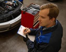 a sobrecarga Visão do automóvel mecânico reparador verificação uma carro motor com inspecionando escrevendo para a prancheta. mecânico manutenção engenheiro trabalhando dentro automotivo indústria. foto