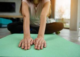 fechar-se do a mãos do uma grávida mulher sentado em uma ioga esteira e alongamento dela corpo enquanto fazendo uma luz exercite-se às lar. fitness, ioga, ativo estilo de vida e gravidez conceito foto