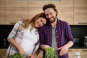 feliz concurso amoroso heterossexual caucasiano casal dentro antecipação em pé fechar para cada de outros enquanto cozinhando saudável jantar às casa cozinha. conceito do maternidade e feliz família relacionamentos foto