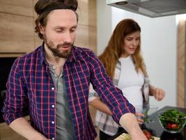 bonito jovem caucasiano homem preparando refeição com dela grávida mulher Fora do foco em a fundo às casa cozinha foto