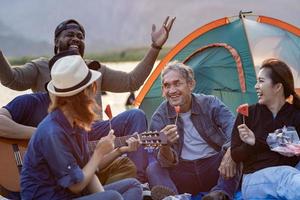 grupo do diversidade amigo e família com crianças apreciar jogando música juntos de a acampamento às a de praia e rindo com felicidade para lazer verão período de férias viagem e ao ar livre viagem conceito foto