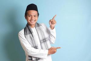 retrato do jovem ásia muçulmano homem mostrando produtos e apontando com dele mão e dedo para a lado. isolado imagem em azul fundo foto
