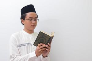 retrato do jovem ásia muçulmano homem lendo e recitando piedosos livro do Alcorão seriamente. isolado imagem em branco fundo foto