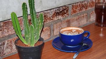 café dentro uma azul xícara, em uma de madeira mesa e uma pequeno cacto foto