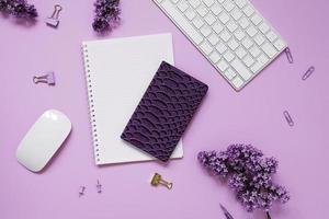 close-up de desktop feminino, teclado, cadernos com caneta, flores lilás. composição plana cortada mínima em um fundo roxo. espaço de cópia foto