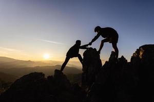 silhueta trabalho em equipe, masculino caminhantes escalada acima montanha penhasco e 1 do eles dando ajudando mão. pessoas ajudando e, equipe trabalhos conceito. foto