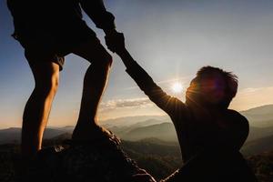 silhueta de alpinista ajudando uns aos outros a subir uma montanha ao pôr do sol. pessoas ajudando e, conceito de trabalho em equipe. foto