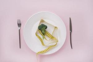 brócolis e fita métrica em um prato no fundo rosa