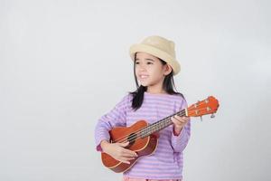 fofa pequeno menina dentro roupa de banho jogando ukulele. feliz período de férias conceito. foto