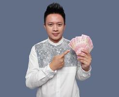 jovem homem segurando e apontando indonésio dinheiro 1 cem mil rupia. foto