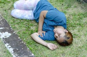 ásia mulher deitado em dela lado desmaio em Relva dentro a parque dentro verão Porque do a quente clima foto