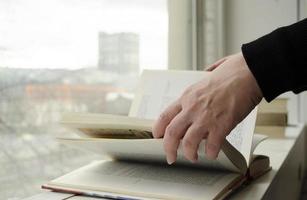 uma pessoa lendo livros perto a janela. mãos voltas sobre livro página. foto