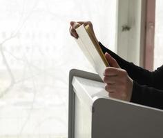 uma pessoa lendo livros perto a janela. mãos voltas sobre livro página. foto