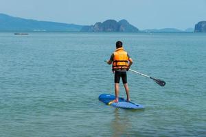 ásia homem jogando sup borda dentro azul mar dentro verão período de férias foto