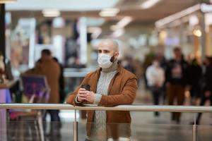 um homem com uma máscara facial está segurando uma xícara de café no shopping foto