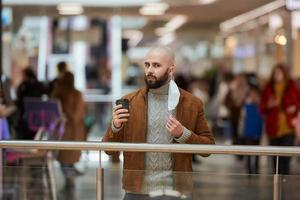 um homem está segurando uma máscara decolada enquanto bebe café no shopping foto