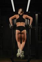 uma foto de trás de uma mulher fazendo flexões nas barras irregulares de uma academia