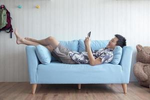 jovem feliz deitado no sofá jogando tablet em casa na sala de estar foto