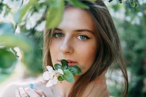 lindo jovem menina dentro uma azul vestir dentro uma florescendo maçã Pomar. florescendo maçã árvores com branco flores foto