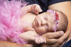uma recém-nascido bebê dorme dentro dele do pai braços. fofa recém-nascido bebê garota. foto