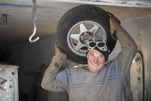 masculino auto mecânico dentro uma garagem com uma carro roda.montagem pneus foto