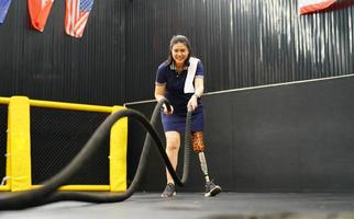 jovem fêmea com 1 protético perna com fazendo braço e ombro exercícios com uma corda para prática balanceamento com protético perna, conceito do vida do mulheres com protético pernas. foto