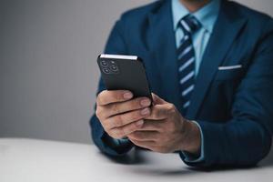 fechar acima Visão do jovem profissional homem de negocios usando Smartphone enquanto sentado às dele escritório escrivaninha. foto