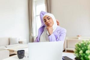 bonita árabe muçulmano senhora com hijab trabalhando às computador portátil sentado às uma mesa às casa - Verifica Fora conectados lojas vendendo cyber segundas - tecnologia mulher conceito para alternativo freelance escritório foto