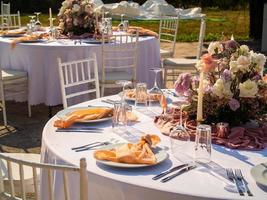 mesa às luxo Casamento recepção evento. lindo flores em mesa e servindo pratos e óculos e decoração foto