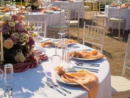 Casamento banquete conceito. cadeiras e volta mesa para convidados, servido com cutler e, flores e louça e coberto com uma toalha de mesa foto