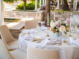 Casamento banquete conceito. cadeiras e volta mesa para convidados, servido com cutler e, flores e louça e coberto com uma toalha de mesa foto