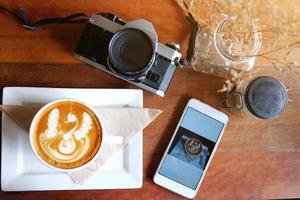 vintage prata filme câmera, decração Smartphone, quente café com leite arte café e seco flores dentro vidro vaso diminuição em madeira mesa, feliz refeição dentro cafeteria às tailândia. foto