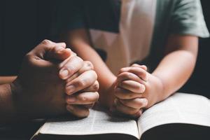 cristão família Rezar juntos conceito. criança e mãe adoração Deus dentro lar. mulher e Garoto mãos Rezar para Deus com a Bíblia implorando para perdão e acreditam dentro bondade. foto