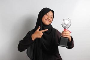 esperto jovem ásia menina aluna dentro hijab apontando dela troféu isolado em branco fundo. foto