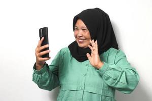 feliz meio envelhecido ásia mulheres vestindo hijab e vestido dentro casual camisa levantando dela mão em vídeo ligar foto