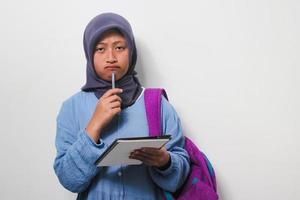 pensativo jovem ásia menina aluna interessado dentro pensando enquanto segurando uma livro e caneta isolado em branco fundo foto
