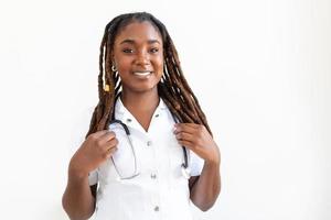 médico sorridente confiante posando e olhando para a câmera com o estetoscópio nas mãos dela. amigável médica afro-americana sorrindo. médico com estetoscópio no pescoço foto