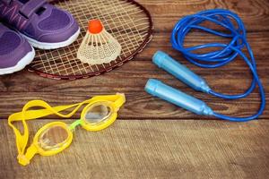 Esportes equipamento a passarinho é em a raquete, saltando corda, natação óculos e tênis em de madeira fundo. tonificado imagem. foto