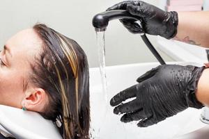 o cabeleireiro em luvas pretas lavando o cabelo da mulher morena no salão de beleza. foto