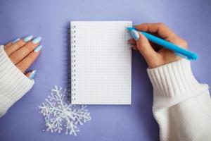 mão de mulher com unhas de inverno segurando caneta no caderno e escrevendo lista de desejos foto