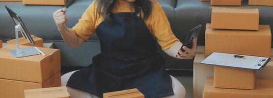 empreendedor de pequenas empresas de startup de mulher asiática freelance usando avental usando laptop e caixa para receber e revisar pedidos on-line para se preparar para embalar vender para clientes, ideias de negócios de sme on-line. foto