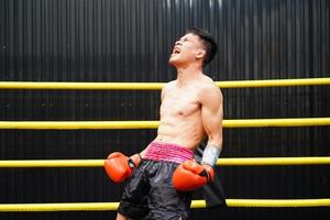 muay tailandês, a marcial arte do tailândia, boxeador felicidade quando ele vitórias de em pé em a boxe anel e gritando satisfatoriamente foto