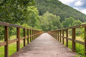 ponte de madeira sobre um campo com prados e colinas arborizadas