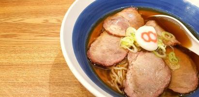 fechar acima quente hachiban ramen macarrão com assado carne de porco fatiado e saboroso sopa dentro azul tigela em de madeira mesa com esquerda cópia de espaço às japonês restaurante. saudável vida estilo comendo e ásia Comida conceito foto