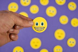 fechar-se tiro do mão segurando amarelo risonho face emoji entre triste emojis em roxa fundo foto