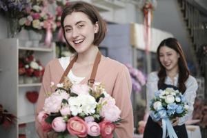 jovem lindo branco fêmea florista trabalhador com grupo do flores e dela colega sorrir e Veja às Câmera às colorida flor fazer compras dentro namorados, pequeno o negócio ocupação, feliz sme empreendedor. foto