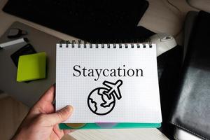 staycation palavra em caderno segurando homem contra Área de Trabalho. foto