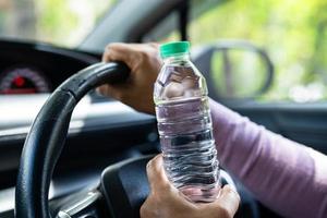 motorista de mulher asiática segurando garrafa para beber água enquanto dirigia um carro. garrafa de água quente de plástico causar incêndio. foto