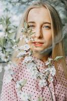 Loiras menina em uma Primavera andar dentro a jardim com cereja flores. fêmea retrato, fechar-se. uma menina dentro uma Rosa polca ponto vestir. foto